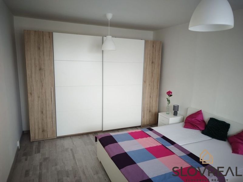 Ložnice s podlahou s dřevěným dekorem v 1+kk bytě, šatní skříň a postel.