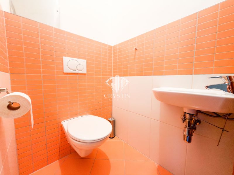 Koupelna ve 3-pokojovém bytě s oranžovými obklady a závěsnou toaletou.