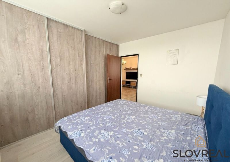 Ložnice s postelí, vestavěnou skříní a průchodem do obývacího pokoje v 3-pokojovém bytě.
