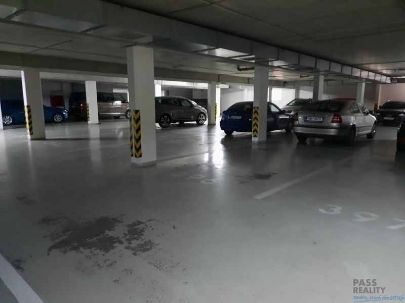 Podzemní garážové stání s parkovanými auty v 2-pokojovém bytě.