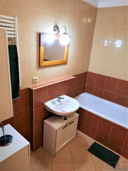 Koupelna s umyvadlem, vanou a skříňkou v 2+kk bytě.