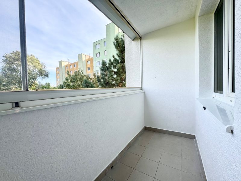 Balkon s dlaždicovou podlahou ve 3-pokojovém bytě, s výhledem na okolní zeleň.