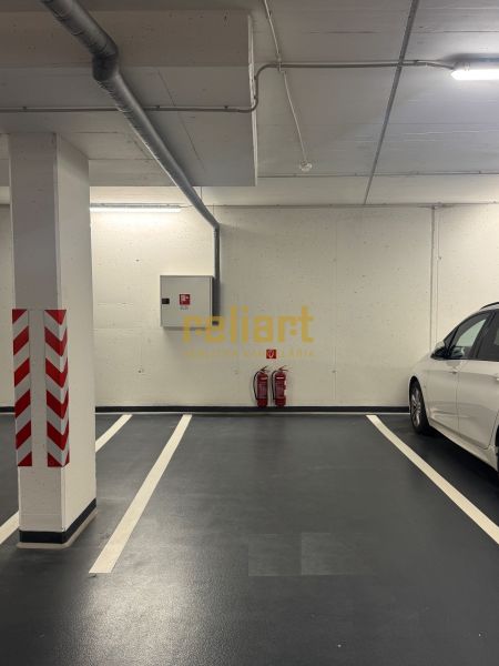 Podzemní parkovací místo s jasným značením a bílým autem vedle.