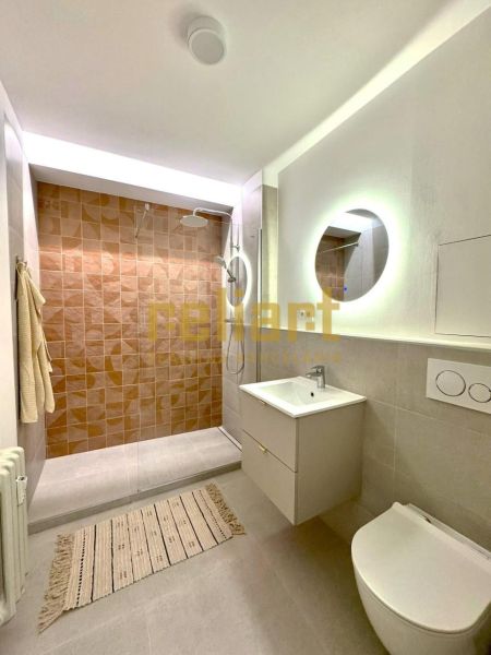 Koupelna s walk-in sprchou, závěsnou toaletou a podsvíceným zrcadlem v 1-pokojovém bytě.
