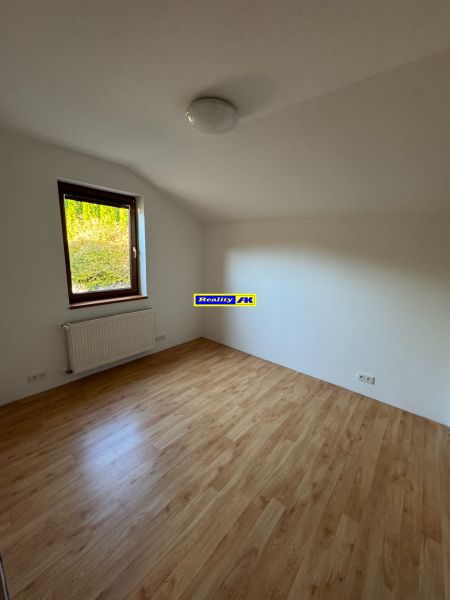 Pokoj v rodinném domě s podlahou s dřevěným dekorem a radiátorem pod oknem.