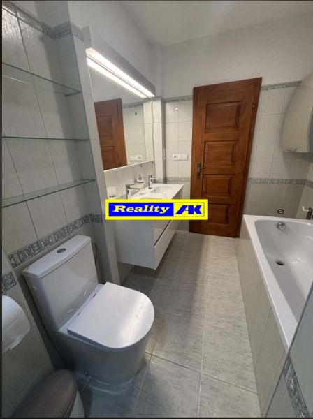 Koupelna s vanou a toaletou v rodinném domě, bílé obklady a dřevěné dveře.