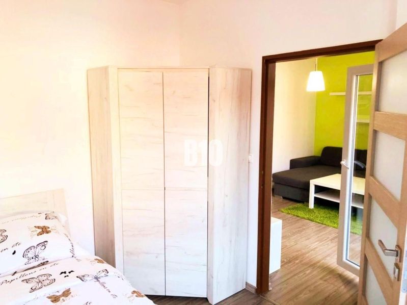 Ložnice s rohovou skříní, vedle vstup do obývacího pokoje s pohovkou.