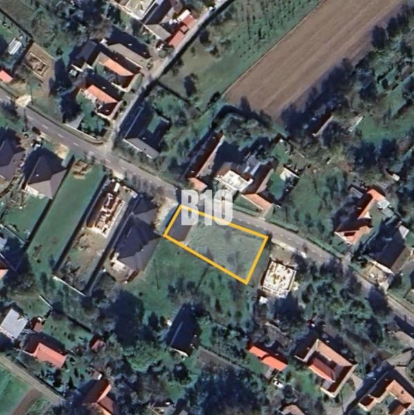 Letecký pohled na pozemek k bydlení v Moravském Lieskovém s viditelnou ulicí a budovami.