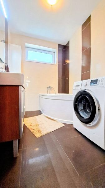 Koupelna v rodinném domě s vanou, pračkou a tmavou dlažbou v dekorativním designu.