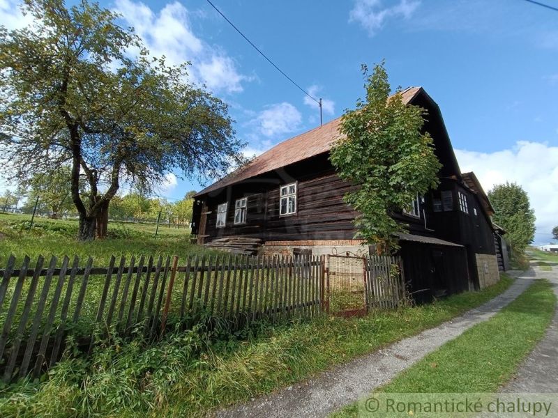 Dřevěná chata ve Staškově obklopená trávou a stromy za plotem.