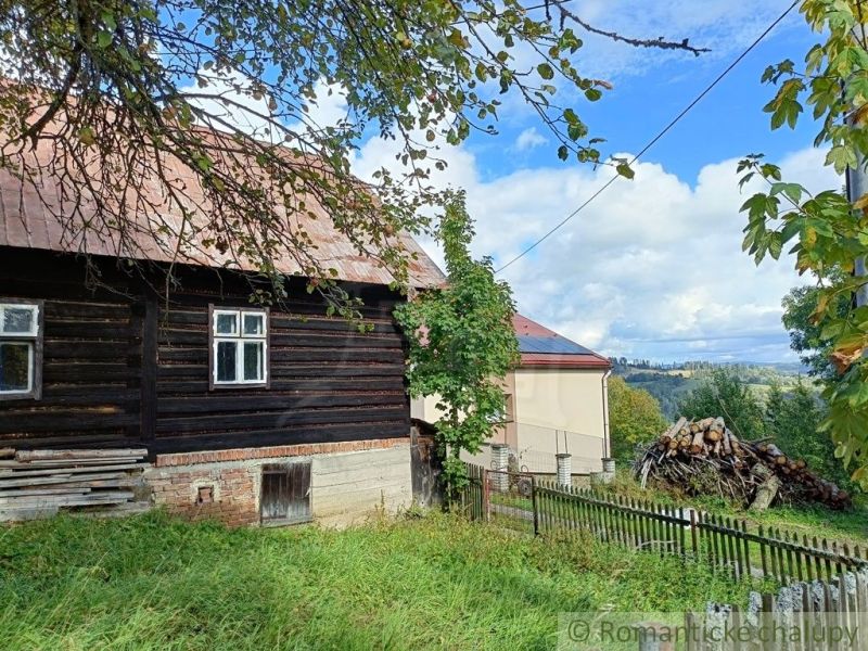Dřevěná chata ve Staškově s ovocnými stromy a výhledem na okolní krajinu.