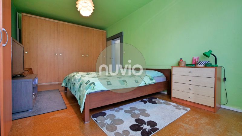 Zelená ložnice ve dvoupokojovém bytě s manželskou postelí, šatníkem a kobercem.